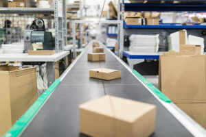 Cajas corrugadas sobre cinta transportadora en depósito de distribución.