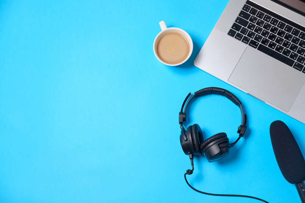 Podcast headphones and microphone on background with computer and coffee cup