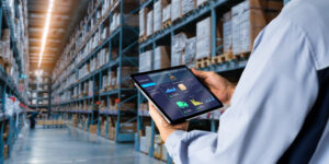 Manager using digital tablet,showing warehouse software management dashboard on blurred warehouse as background