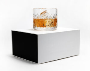 Rocks glass filled with amber liquid sitting on a white and black luxury box