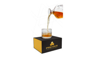 Bourbon being poured into a rocks glass on top of a Premier Packaging black luxury box.