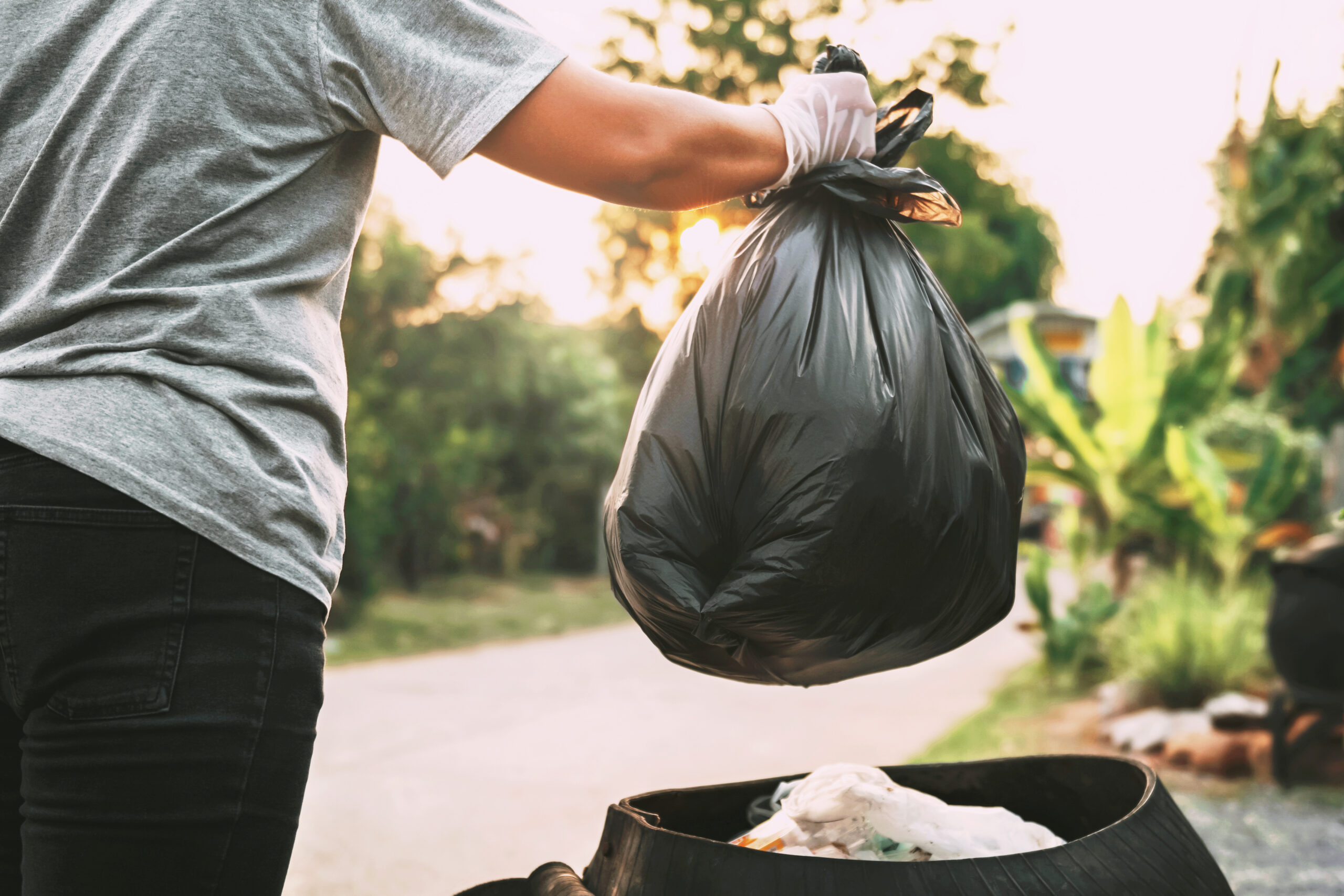 Mano arrojando una bolsa de basura negra en un contenedor de residuos en el exterior