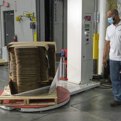 Stretch Wrapper being ran by employee to wrap boxes Premier Packaging employee managing stretch wrapper machine; Warehouse equipment; packaging equipment; packaging automation equipment